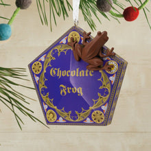 Load image into Gallery viewer, Ornament shaped like a chocolate frog on a string with green leaves in the background