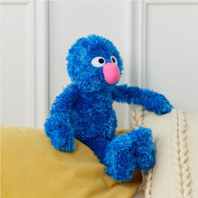 Load image into Gallery viewer, Sesame Street Grover Blue plush toy with a pink nose sitting on a yellow surface against a white paneled wall.
