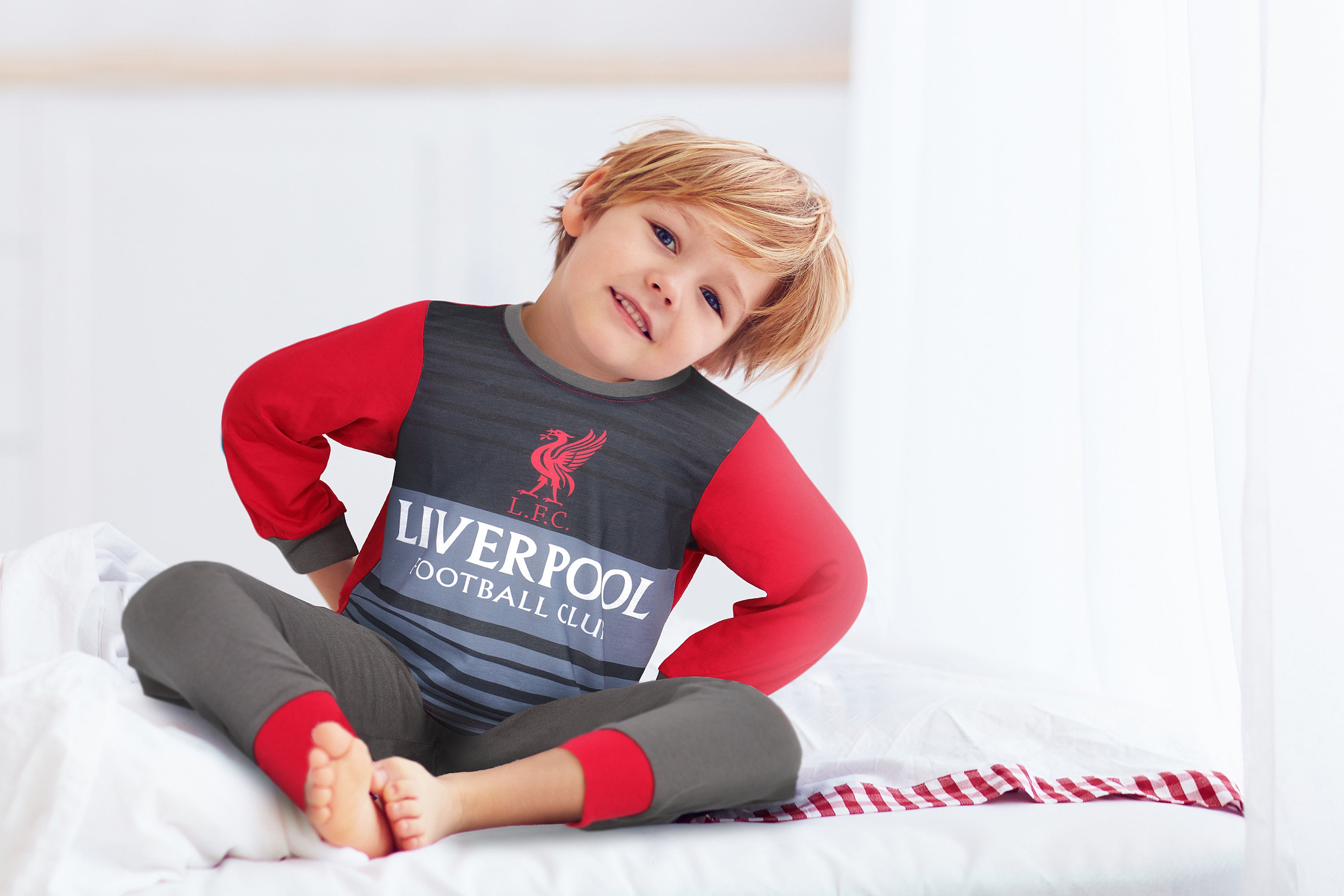 boy toddler aged 5 yerars sitting on bed wearing Liverpool Football Club Pyjamas